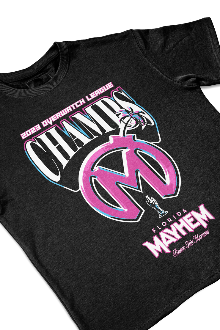  A heathered gray short-sleeved t-shirt showcasing a vibrant design. The graphic emphasizes "2023 Overwatch League CHAMPS" in bold pink, black, and cyan colors. Beneath this, a stylized Florida Mayhem logo in pink and cyan, designed to resemble a bomb, dominates the center. The phrase "Florida Mayhem" appears in a striking pink font below the logo, with a small mascot icon positioned just above the t-shirt&